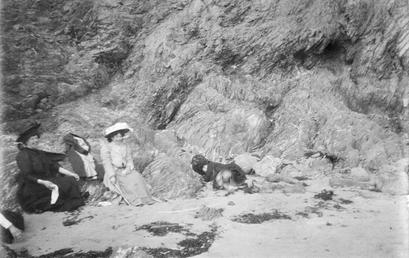 Two woman sitting on rocks below a cliff,…