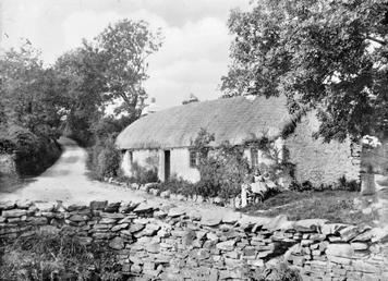 Thatched cottage with two children seated outside, possibly…