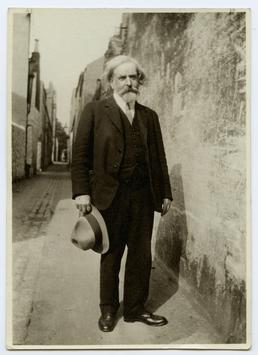 Archibald Knox standing in narrow lane behind 70…