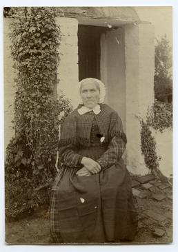 Unidentified woman seated in front of doorway to…